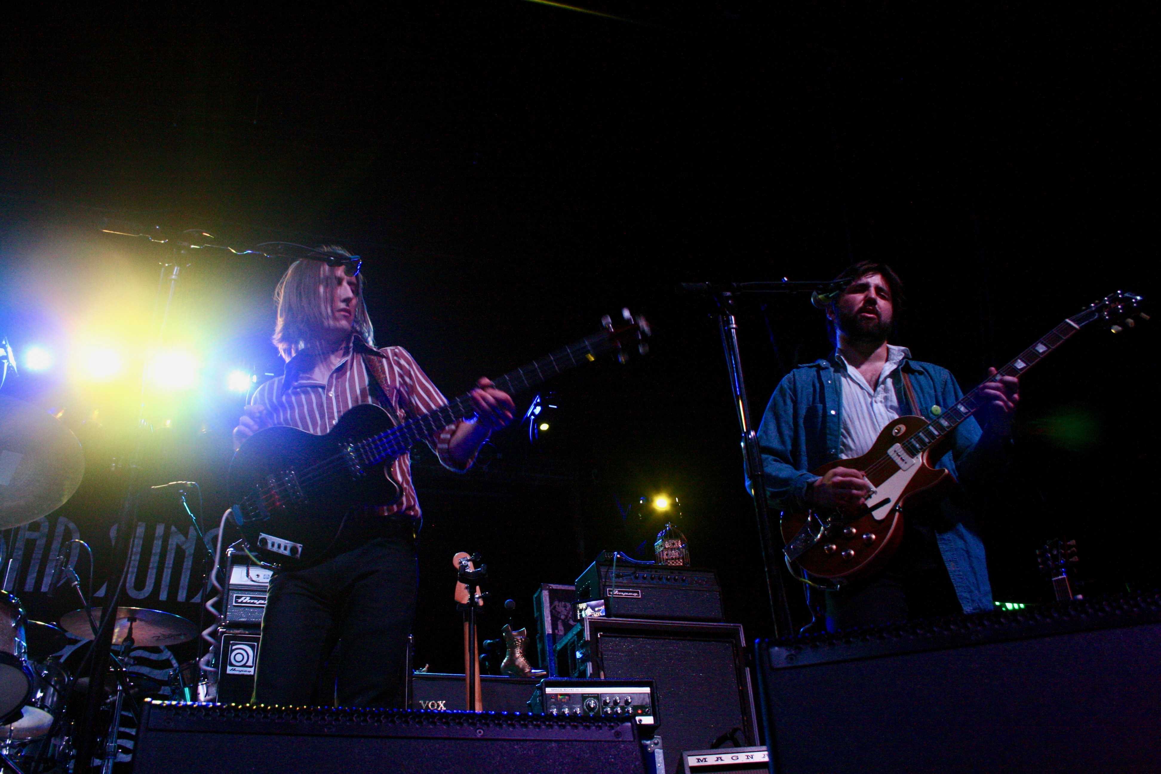 Two young men on stage strum guitars.