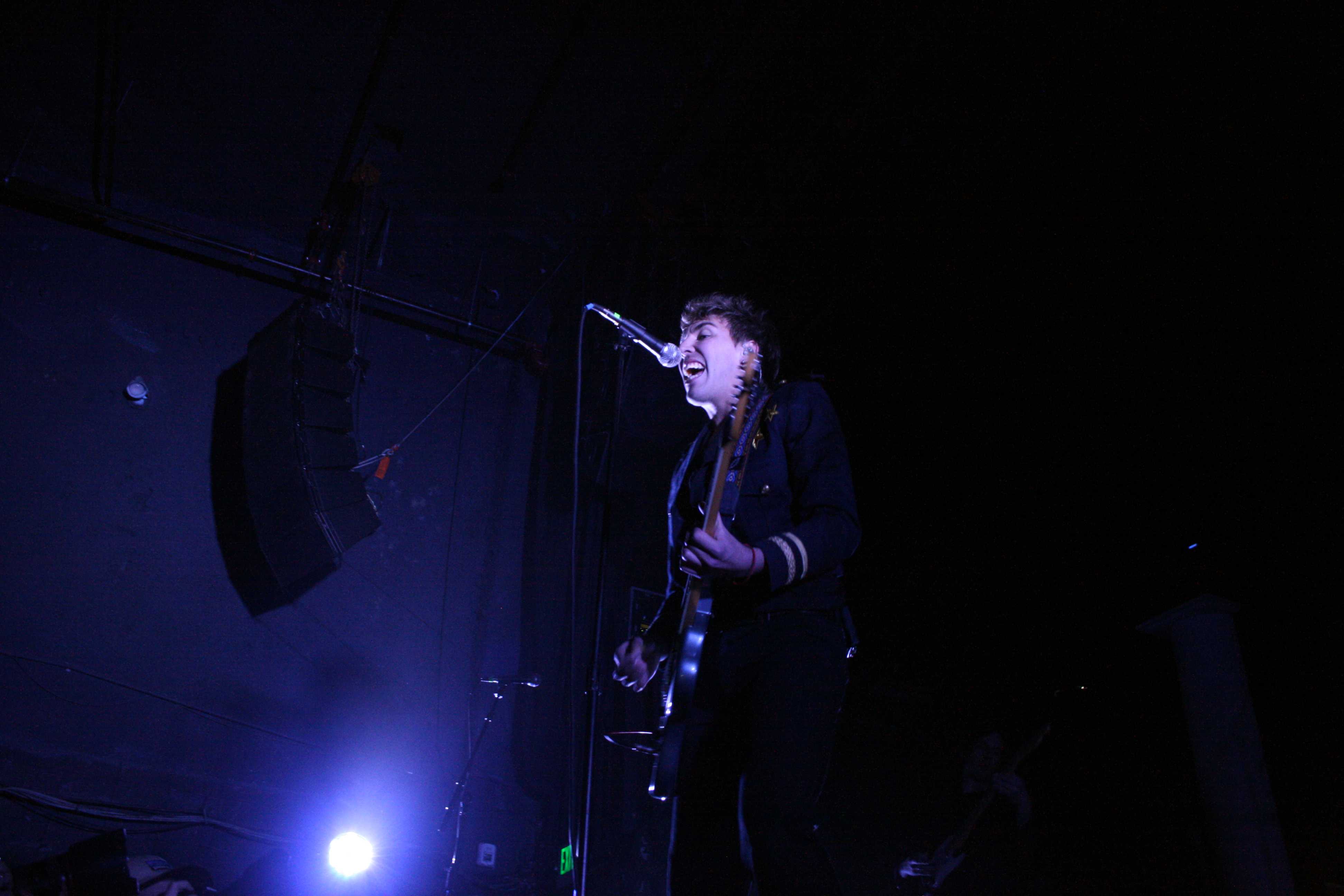 Young man on stage strums guitar.