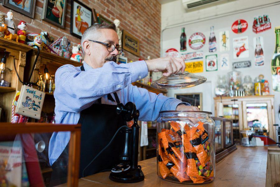 Tony Vallejos, owner of The Fort Collins Candy Store Emporium, reaches into a jar of his favorite candy inside his quirky, old-school shop. Originally from California, Vallejos is a retired interior designer who pursued his childhood dream of opening a candy store. His favorite candies are Licorice Duos, a chewy piece of licorice mixed with a fruit gummy. (Brooke Buchan | Collegian). 