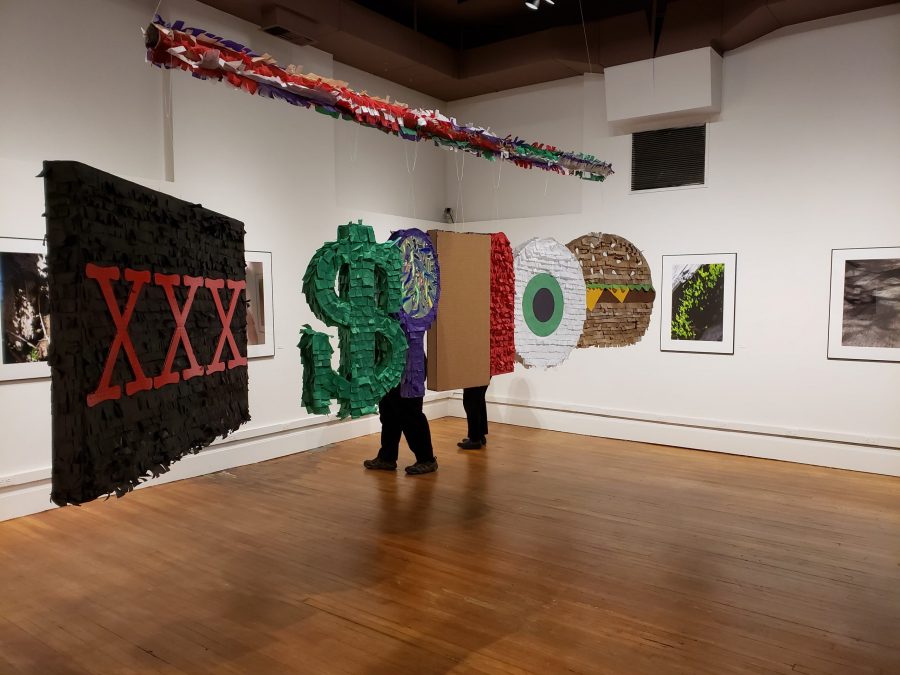 Piñatas representing the seven deadly sins created by Saxon Martinez hang in the center of the Carnegie Center for Creativity, surrounded by macro photography by Maranda Hutson (Graham Shapley | Collegian)