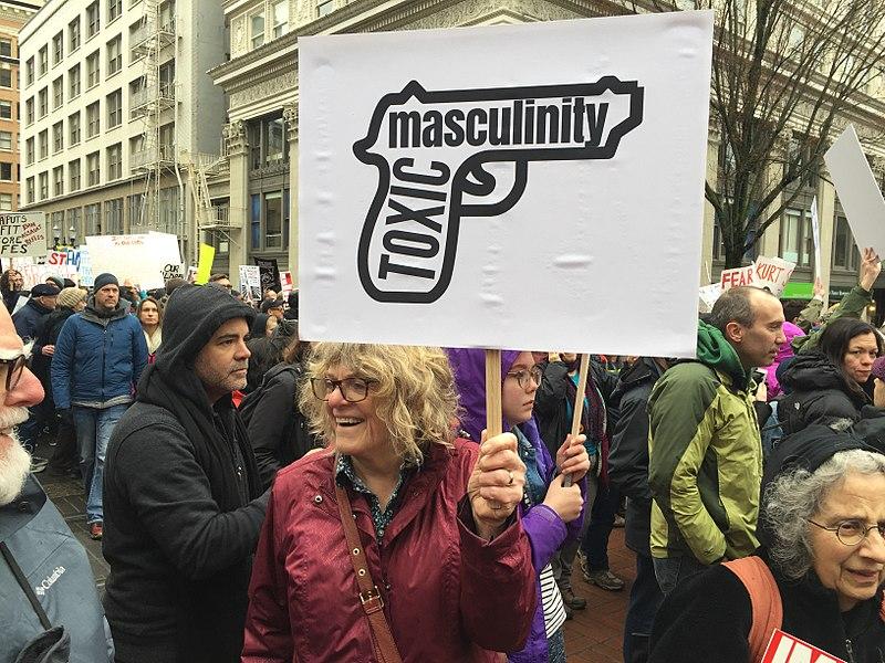 A women holding a sign that reads "toxic masculinity" inside a drawing of a gun