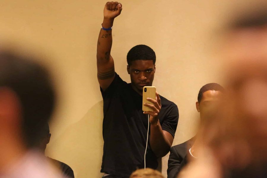 A gallery member holds up his fist and records the speaker on his phone at the Associated Students of Colorado State University senate session Sept. 18, 2019, during a discussion of the blackface image that has been circulating on social media recently. The senate session was moved to the North Ballroom of the Lory Student Center to a accommodate for an unusually large crowd size. (Forrest Czarnecki | The Collegian)