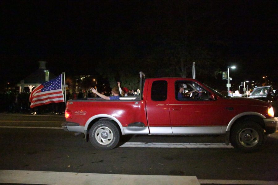 A truck decked out in American flags and other conservative paraphernalia drives past the protesters at the Charlie Kirk Culture War event at the University Center for the Arts Oct. 22, 2019. The event featured both Charlie Kirk, a prominent conservative speaker, and Donald Trump Jr., where they discussed conservative values and socialism in the U.S. (Forrest Czarnecki | The Collegian)
