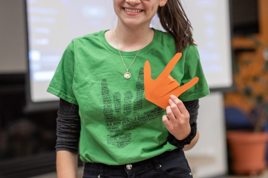 Junior Liberal Arts student Lu Epstein holds up a paper hand signing, "I love you," during the Smile event at the International House Thursday, Oct. 24. The paper hands are intended to be pinned to shirts in order to show solidarity with speakers of sign language. (Brooke Buchan | The Collegian).