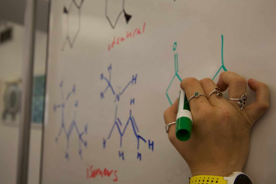 Woman draws chemistry diagrams on a whiteboard. (Photo Illustration by Ryan Schmidt | The Collegian)