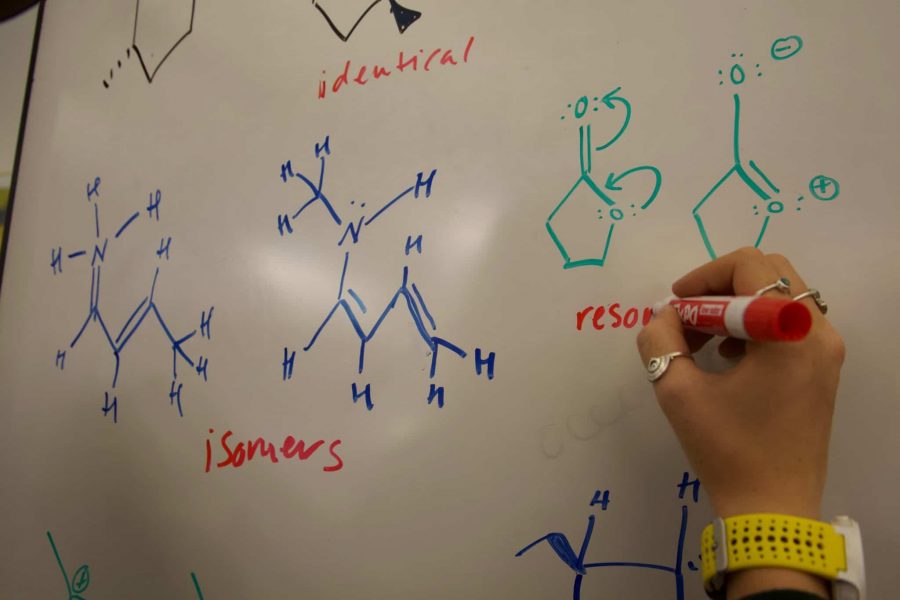 Woman draws chemistry diagrams on a whiteboard. (Photo Illustration by Ryan Schmidt | The Collegian)