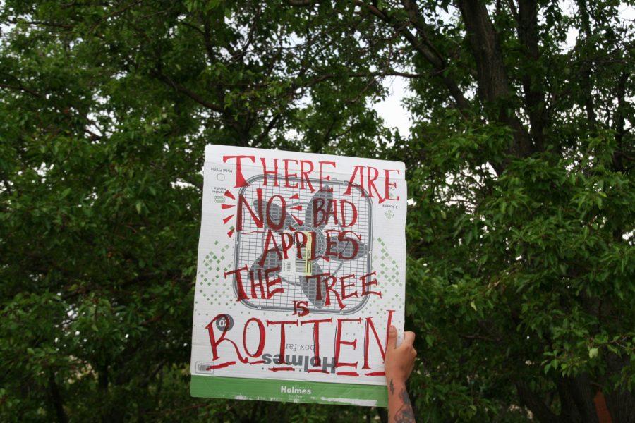 A protestor holds up a sign outside the Aurora Municipal Center on June 27. The sign refers to the saying that often with police there are, a few bad apples. (Katrina Leibee | The Collegian).