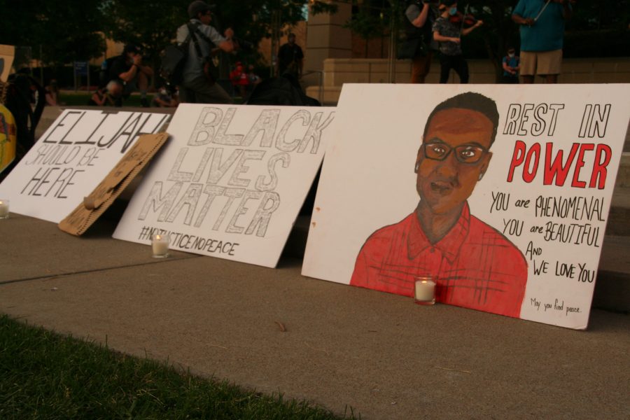 Protestors placed their signs around along with candles to host a vigil for Elijah McClain. Musicians play their string instruments on the stage above. (Katrina Leibee | The Collegian)