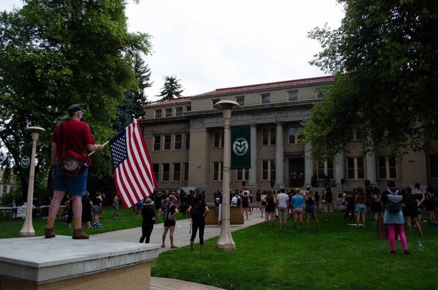 A man with an upside down American flag stands on a pillar outside the Colorado State University Administration Building. (Reed Slater | The Collegian)