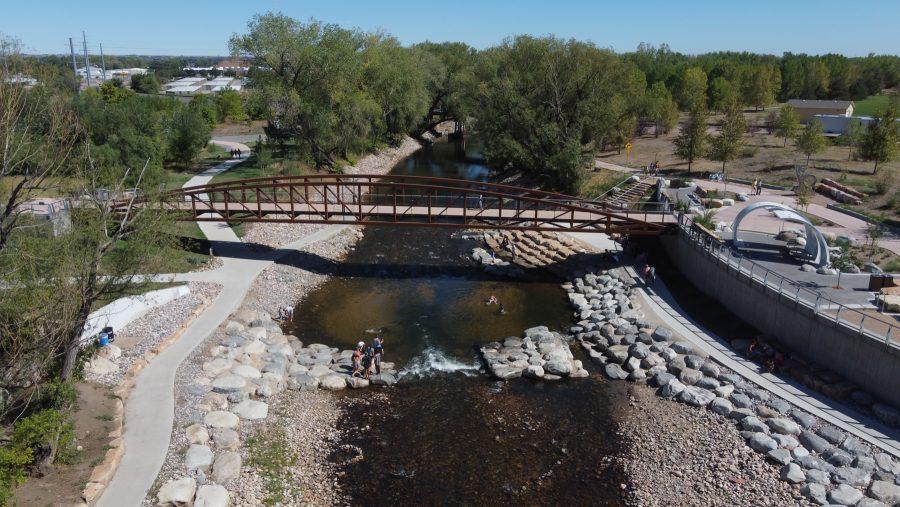 People stand next to the Poudre River at the Fort Collins Whitewater park during the day. The Park sits right next to the Colorado State University Powerhouse Energy Campus. Visitors can swim and tube down the rapids. (Devin Cornelius | Collegian)