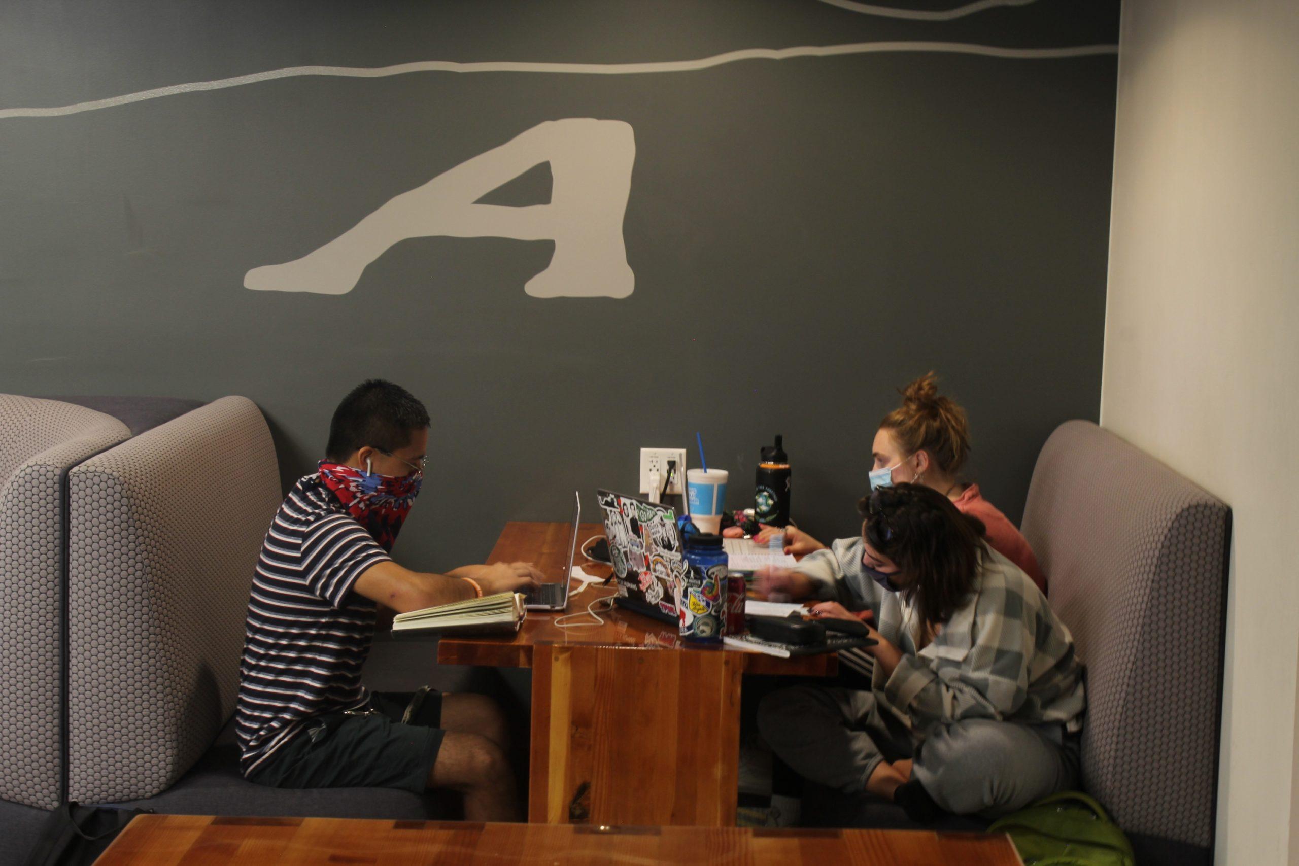 three students sit in a booth studying