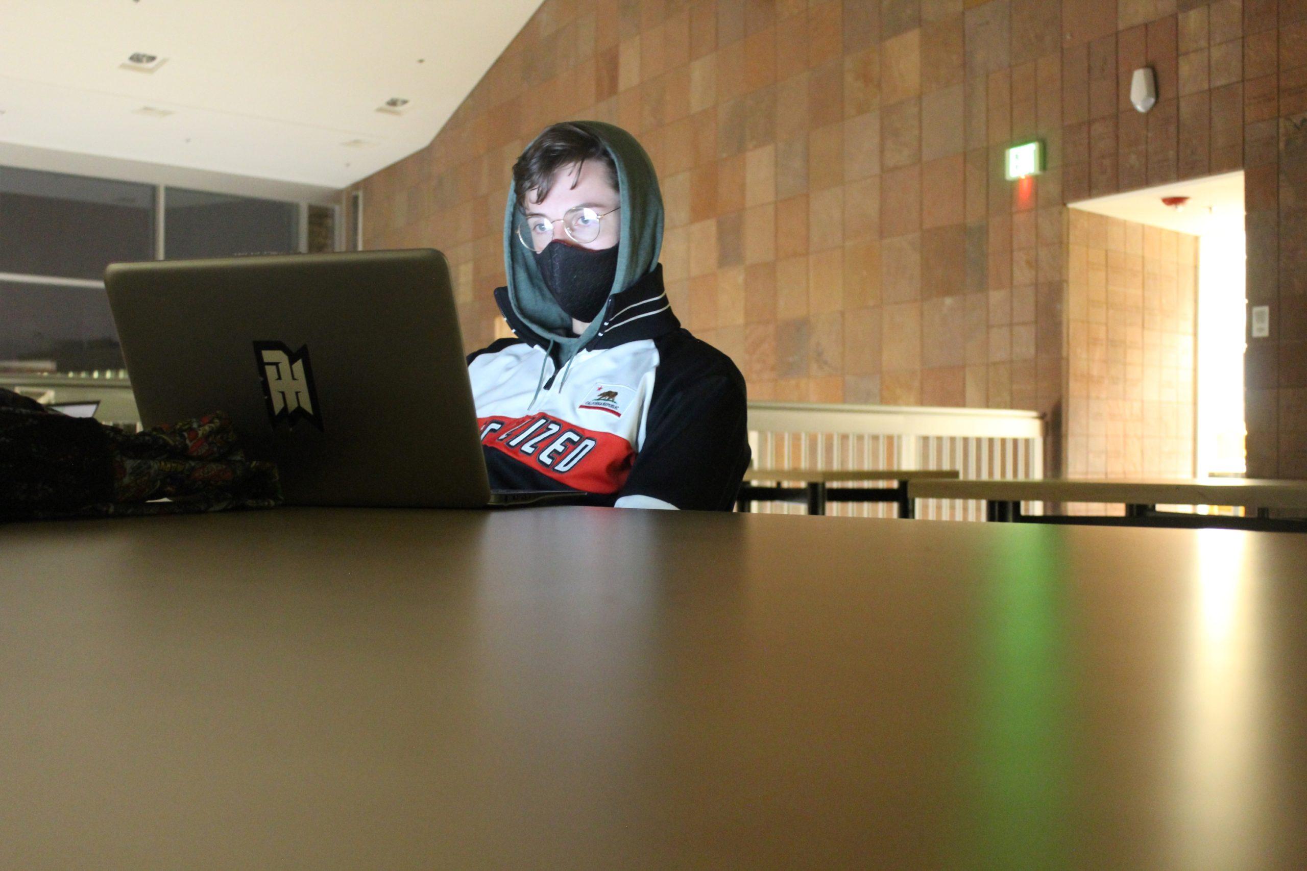 man wearing glasses and a mask stares at a laptop
