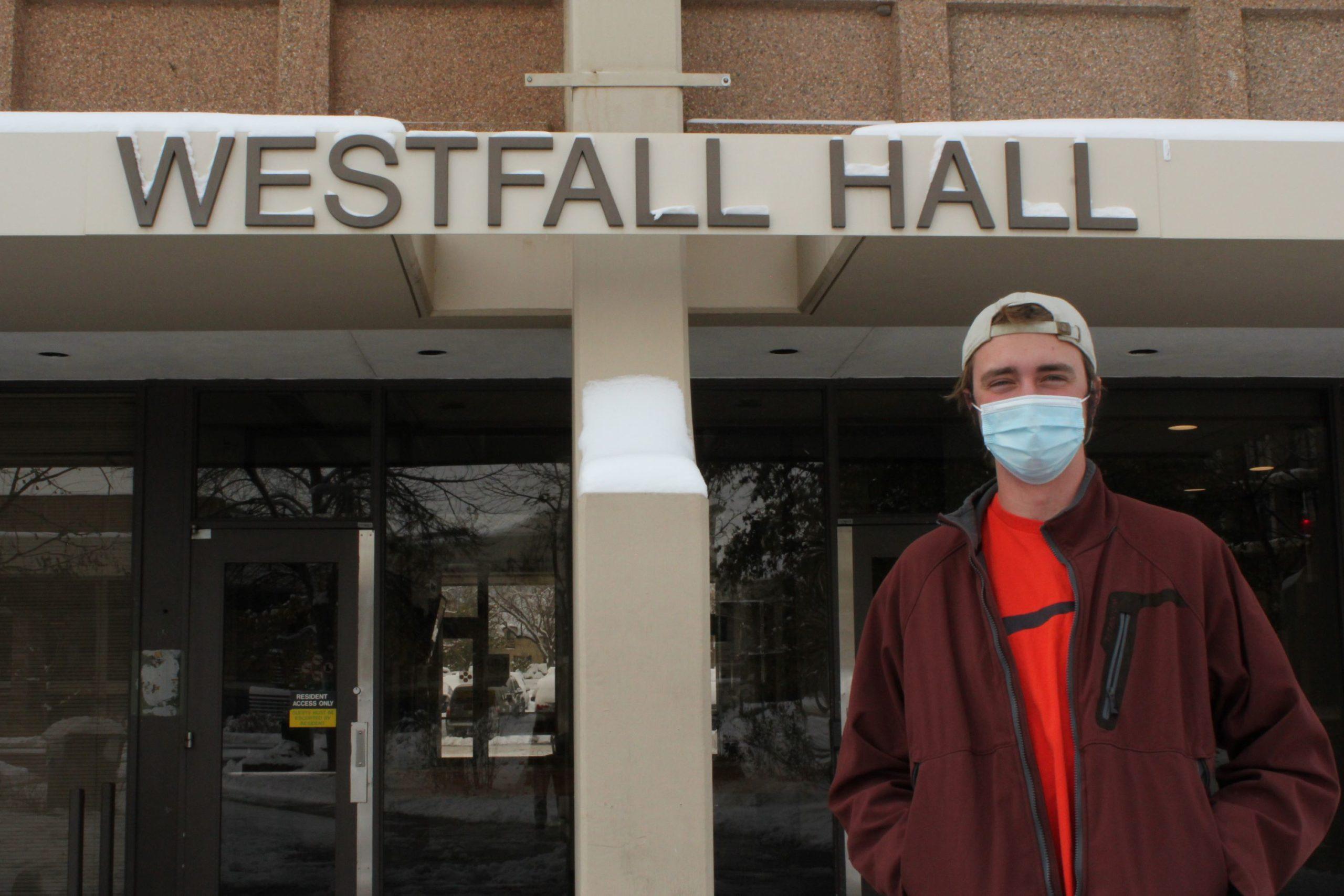 student stands in front of dorm with mask