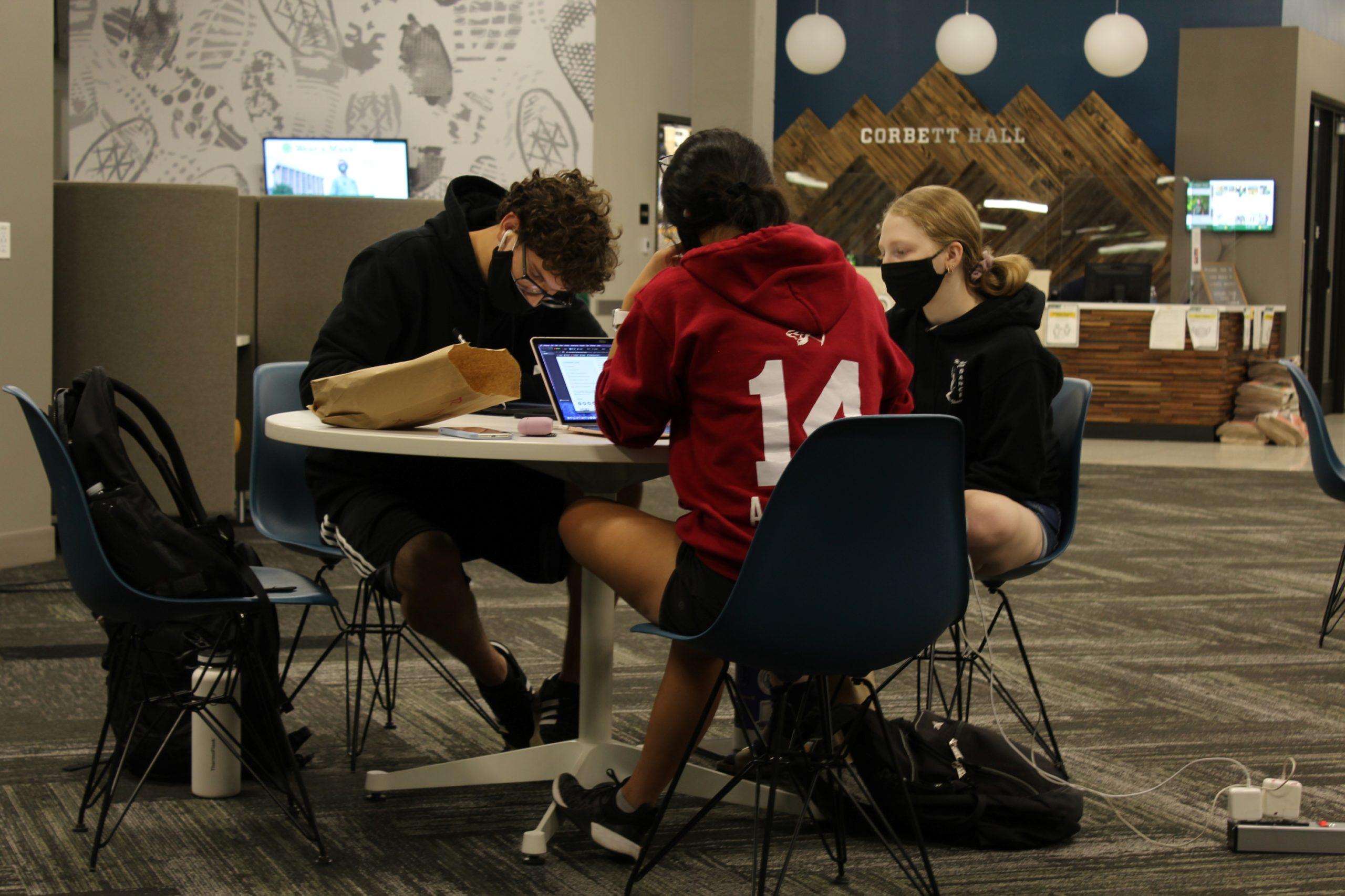three students sit at desk studying