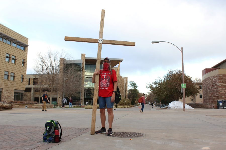 Cherie Circenis stands with a wooden cross awaiting discussion regarding religion and other politically-based topics on the plaza at Colorado State University on election day, Nov. 3. (Cat Blouch | The Collegian)