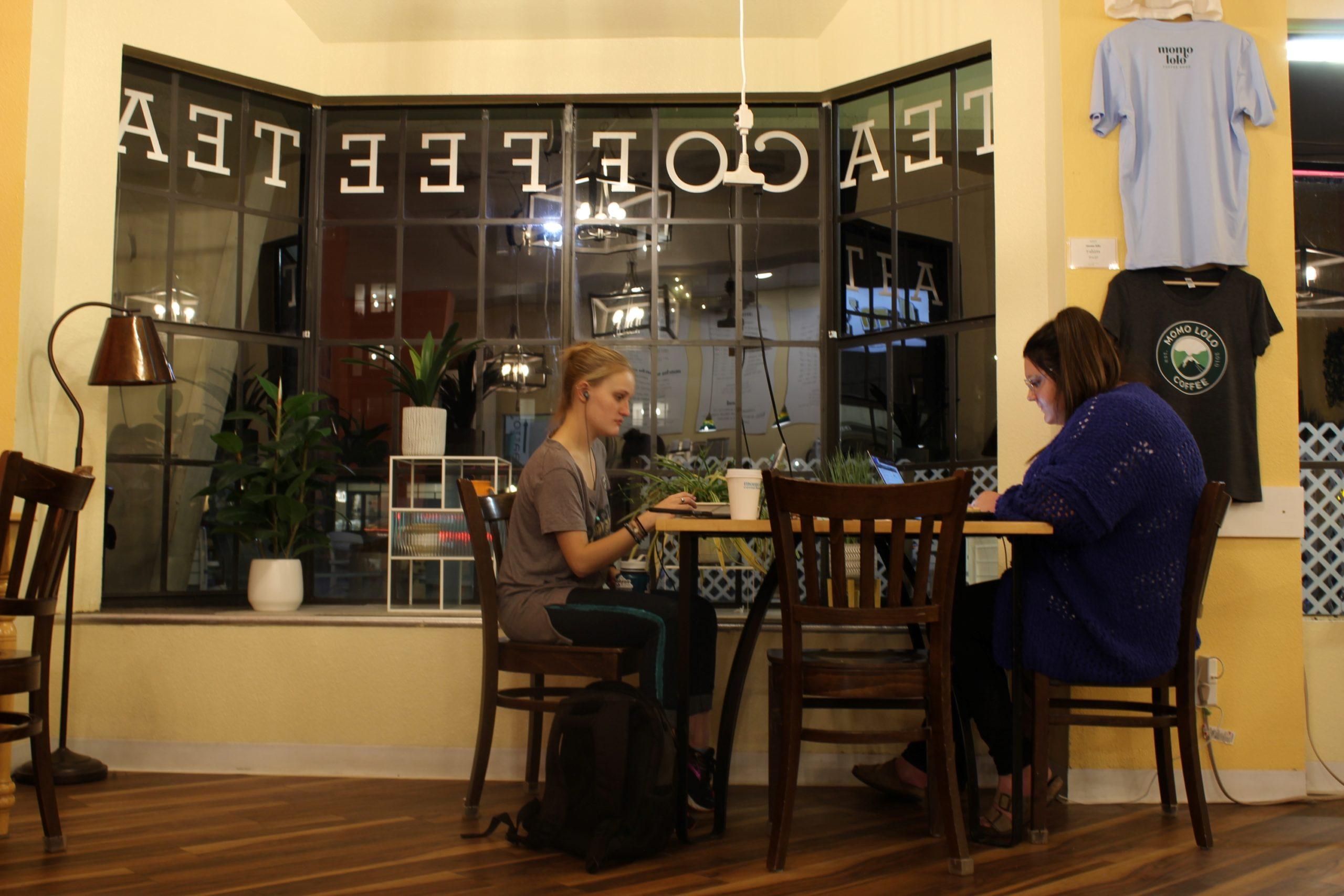 two girls sitting at a coffee shop doing homework