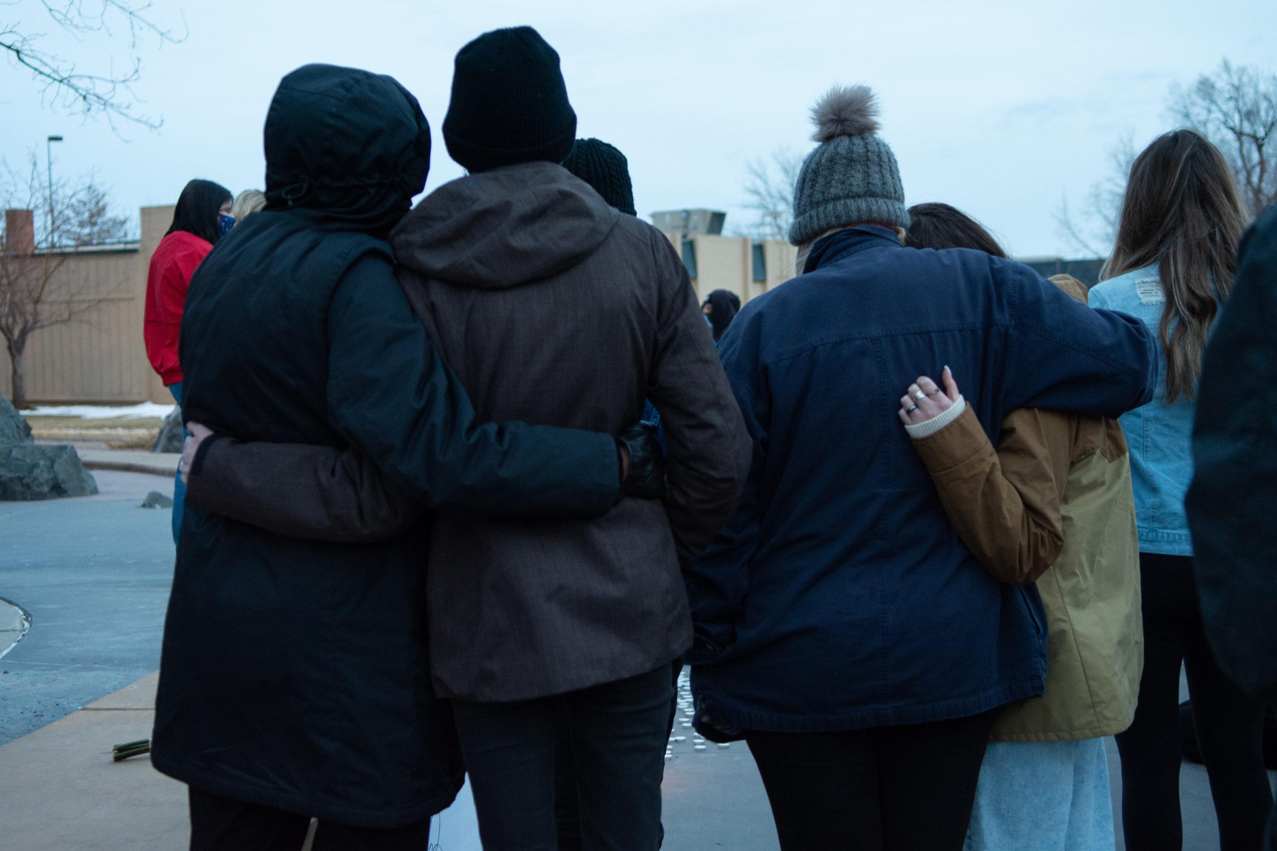 photo of the backs of people standing outside and with arms around one another