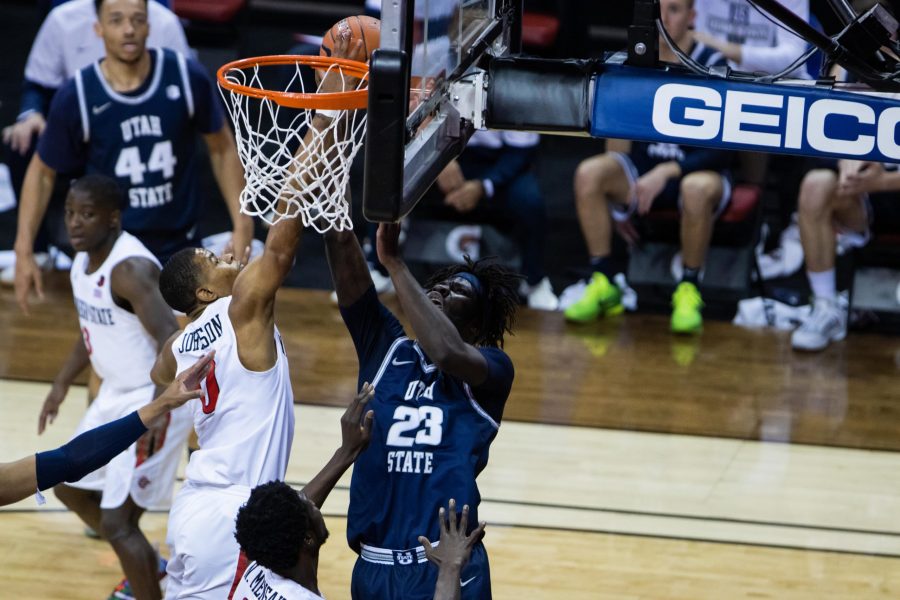 Two basketball players from opposing teams jump for the ball at the hoop.