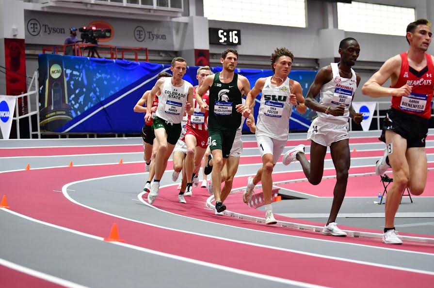 A group of men are running around a corner on an indoor track.