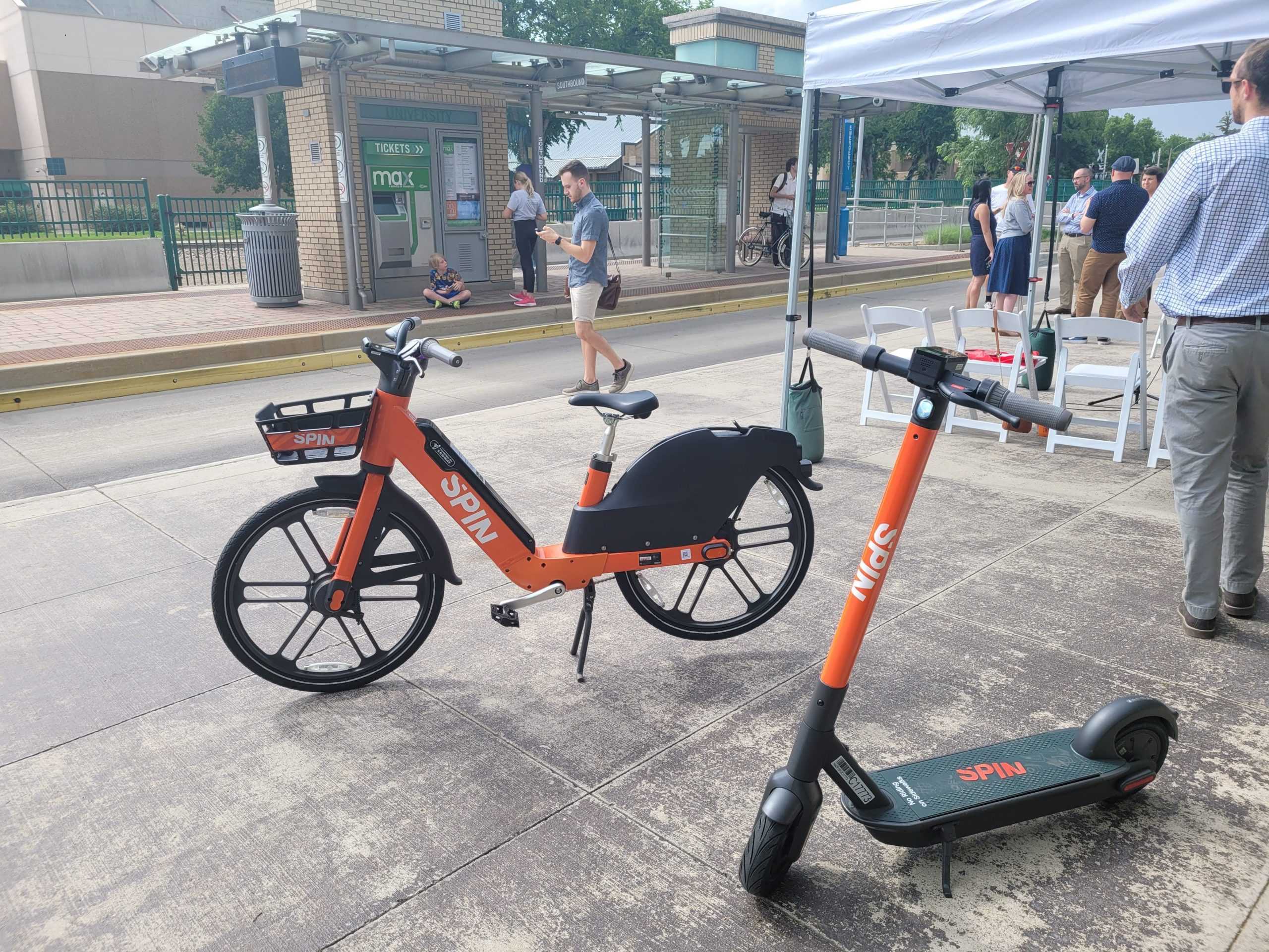 An organge electric bike and an orange electric scooter sit on a sidewalk for display.
