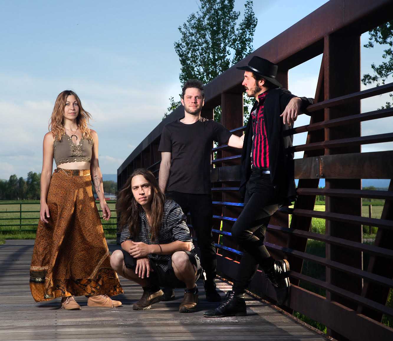 Four people stand on a bridge, with green grass and trees behind a fence in the background.