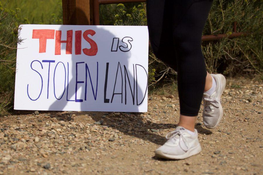 A hiker at the Maxwell Natural Area passes a sign placed by the First Nations Right Relations Gathering for Hughes Land Back Aug. 22. Colorado State University planned to develop the Hughes land, but activists hoped the site could be used as a gathering place for Indigenous people.