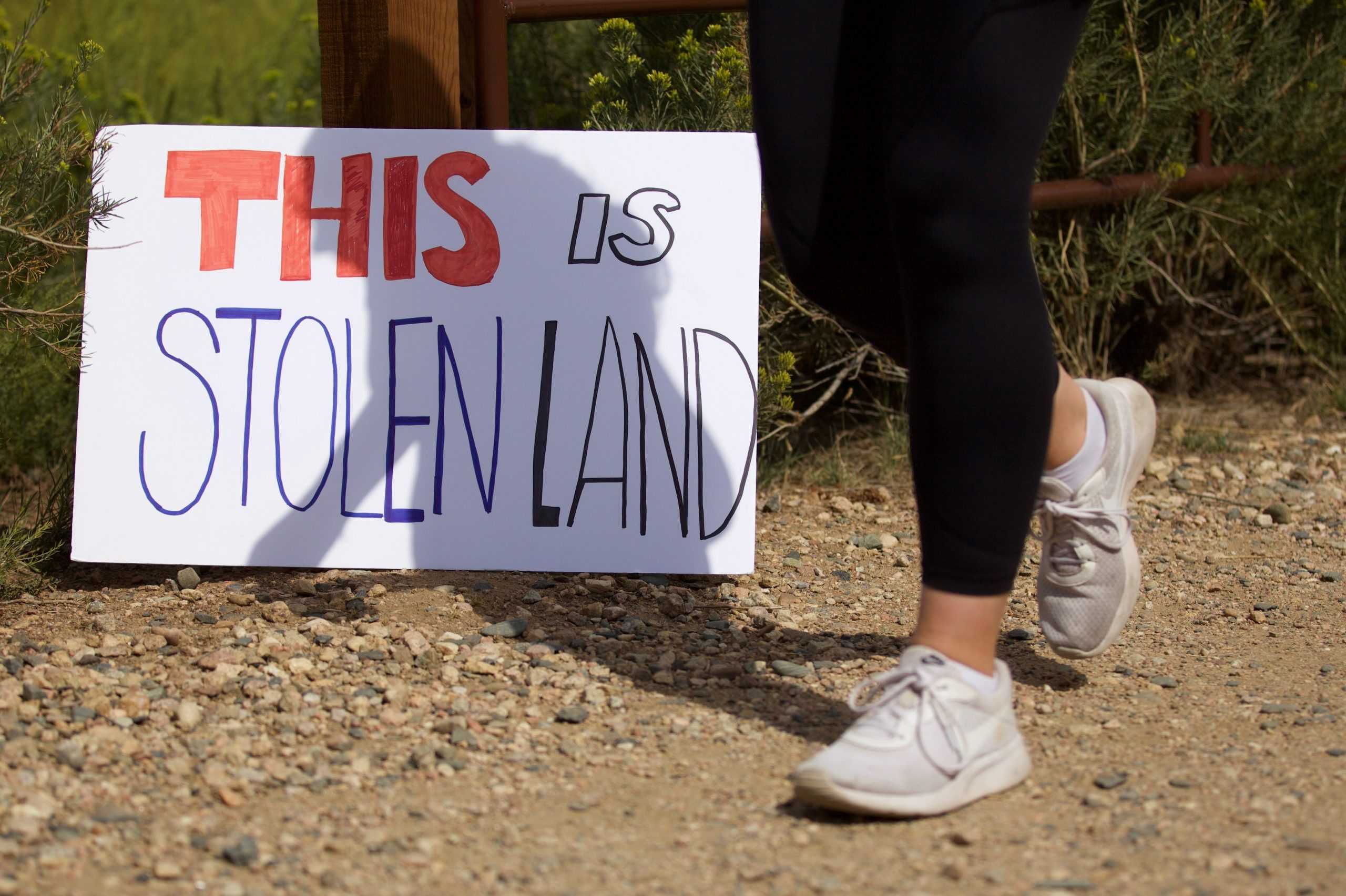 A person walks past a sign that reads "THIS IS STOLEN LAND"