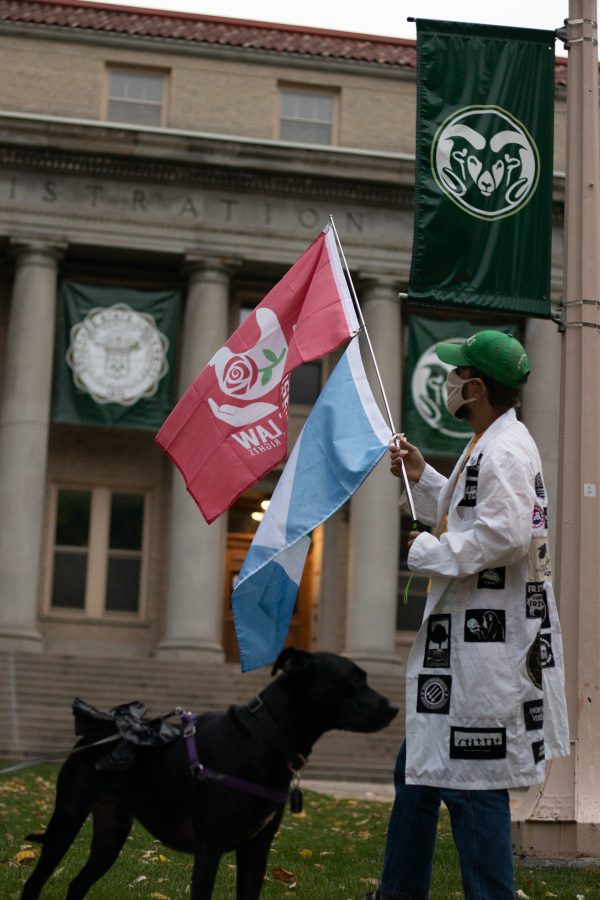 Lied Youngs, Climate change protestor, waves Rose’s Law flag (an animal rights group), with a dog named Nochi, in front of the Administration building at Colorado State University Oct 08. The protest was based around a cleaner campus and the equal pay to the working students who are overburdened. (The Collegian | Grayson Reed)