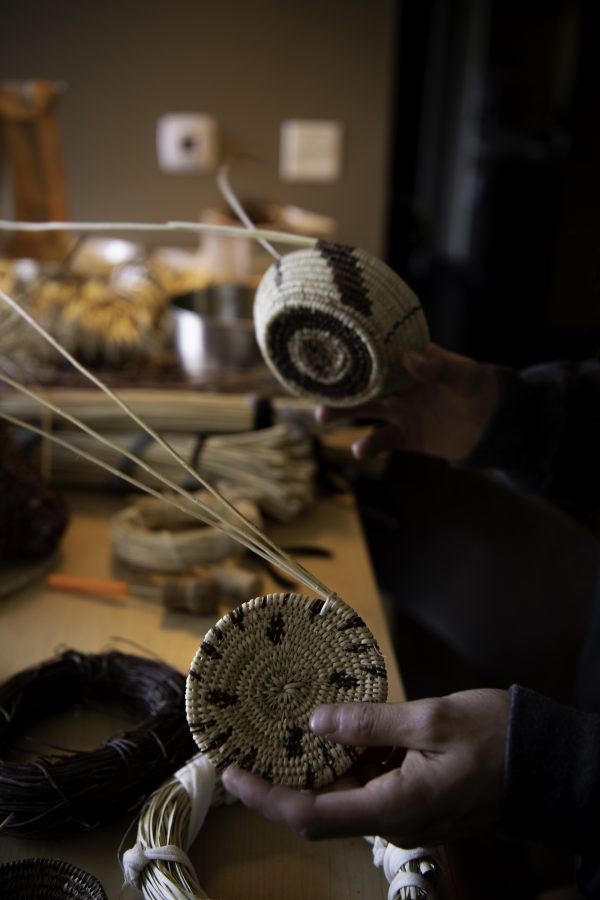 Stephen Young of the Mountain Maidu tribe holds two of his hand-woven baskets in his apartment on Colorado State University campus Oct. 12. The bottom one will be a 16-inch-wide Milky Way patterned tray and the top will be a bird flock pattern. (Garrett Mogel | The Collegian)