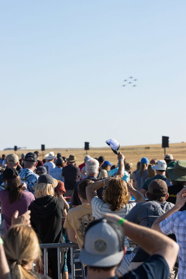 A spectator tips their cap towards the approaching Blue Angels flying in formation