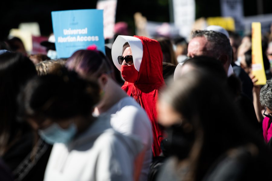 A protester dressed as a handmaid from Margaret Atwood’s 1985 fictional dystopian universe watches speakers outside of the Colorado State Capitol at the Denver Women’s March Oct. 2. (Lucy Morantz | The Collegian)