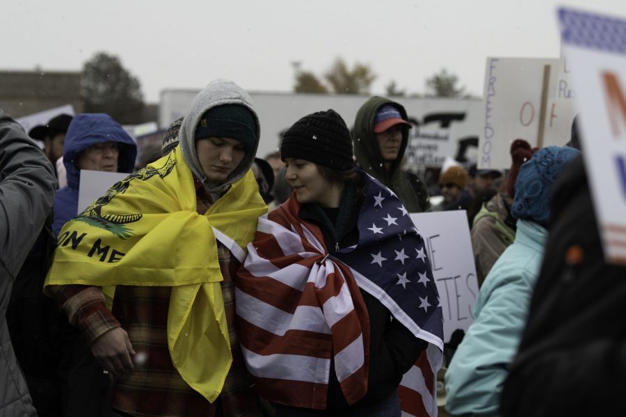 Two people wrapped in flags stand in the snow at a rally against vaccine mandates Nov. 1. The rally took place outside the Larimer County Health Offices, 1525 Blue Spruce Drive Fort Collins Colorado with approximately one thousand to two-thousand attendees. (Garrett Mogel | The Collegian)