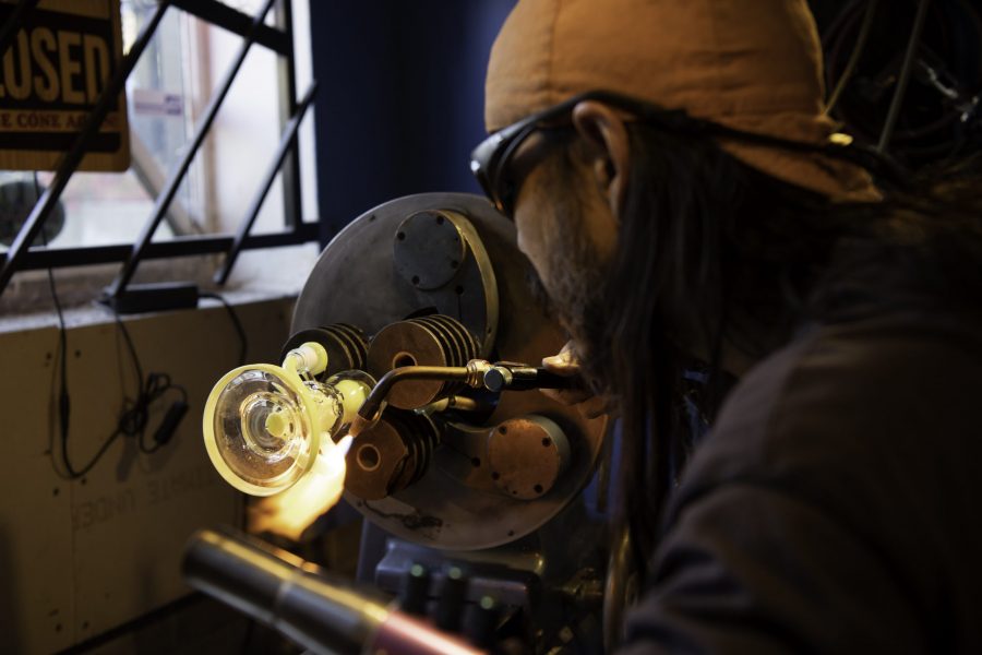 En-tao Andrew Hsu, artist name Torch Mouth repairs a cracked bong on a lathe inside Kind Creation Fort Collins Colorado Nov. 3. Torch Mouth comes from the fabricated helmet he wears for demonstrations that features a torch in the mouth.(Garrett Mogel | The Collegian)