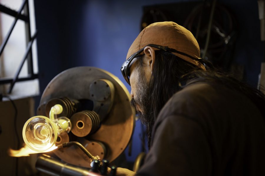 En-tao Andrew Hsu, artist name Torch Mouth repairs a cracked bong on a lathe inside Kind Creation Fort Collins Colorado Nov. 3. Torch Mouth comes from the fabricated helmet he wears for demonstrations that features a torch in the mouth. (Garrett Mogel | The Collegian)