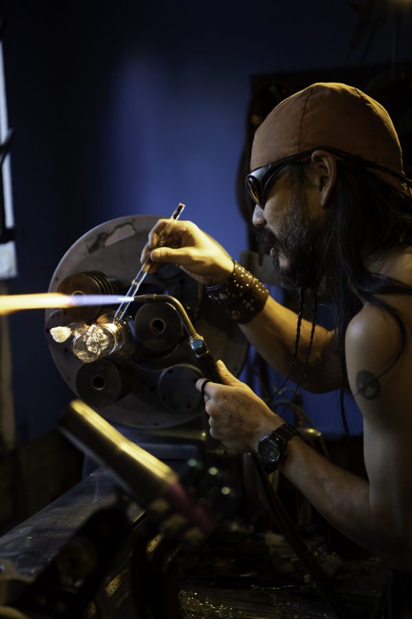 En-tao Andrew Hsu, artist name Torch Mouth repairs a cracked bong on a lathe inside Kind Creation Fort Collins Colorado Nov. 3. Torch Mouth comes from the fabricated helmet he wears for demonstrations that features a torch in the mouth. (Garrett Mogel | The Collegian)