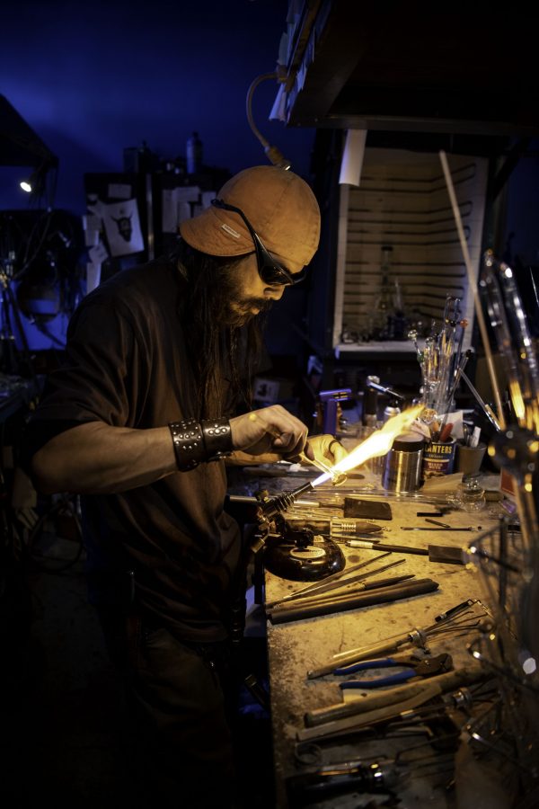 En-tao Andrew Hsu, artist name Torch Mouth repairs a cracked bong on a lathe inside Kind Creation Fort Collins Colorado Nov. 3. Torch Mouth comes from the fabricated helmet he wears for demonstrations that features a torch in the mouth. (Garrett Mogel | The Collegian)