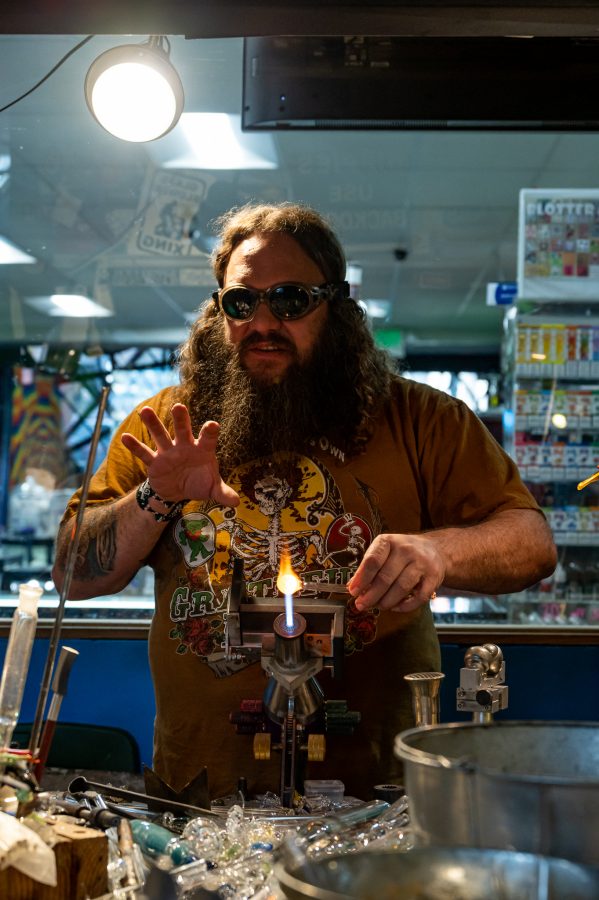 Sky Norton heats up glass at Kind Creations Nov. 9. Norton wanted to start blowing glass when, "I was on dead tour in the 90's and saw people pulling up in their buses with makeshift glassblowing stations." (Milo Gladstein | The Collegian)