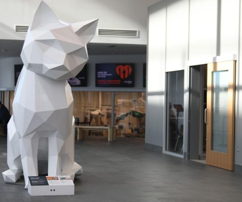 A white sculpture of a cat sits in the lobby of a building.