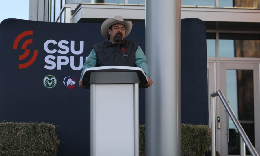 A+man+in+a+cowboy+hat+stands+behind+a+silver+podium+in+front+of+a+sign+that+reads+CSU+Spur.