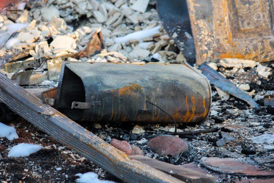 A rusted, melted mailbox lays among the rubble of a burnt home.