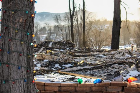 Christmas lights are strung up on a tree trunk, untouched, with fallen melted Christmas decorations among the houses rubble.