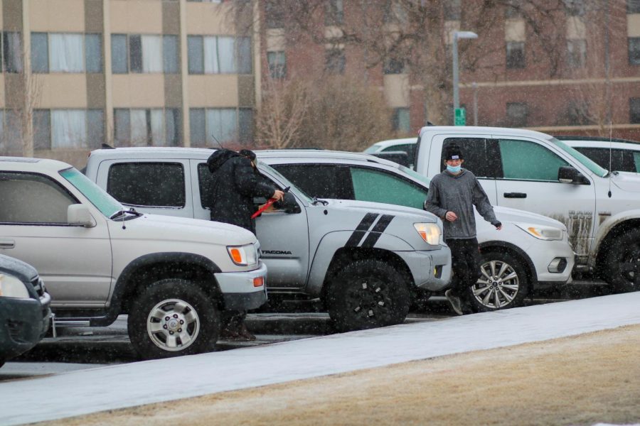 Two students scrape the ice off of their car.