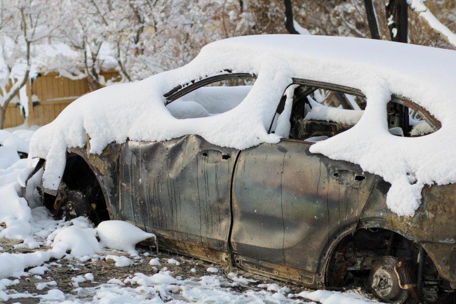 A charred car sits under a blanket of snow.