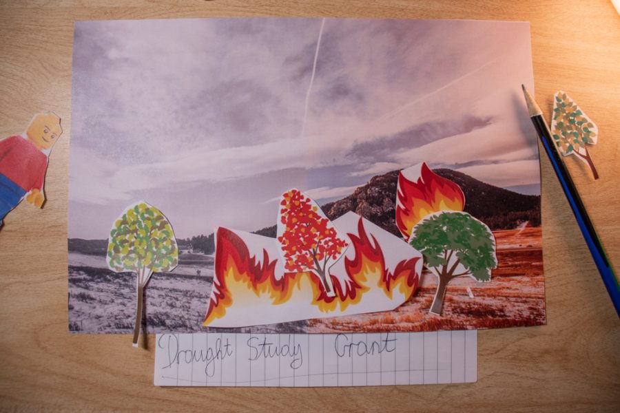 A picture of a landscape placed on top of a desk with cut-out pictures of illustrated fire and trees placed on top.