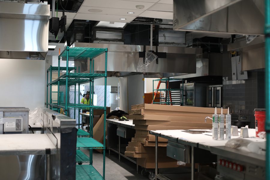 An industrial kitchen that has empty shelves, cardboard boxes and is still partially under construction