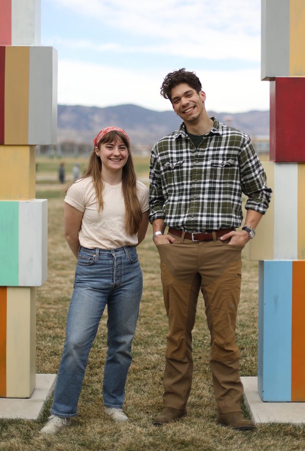 Two people stand outside, smiling, in between two colorful pillars
