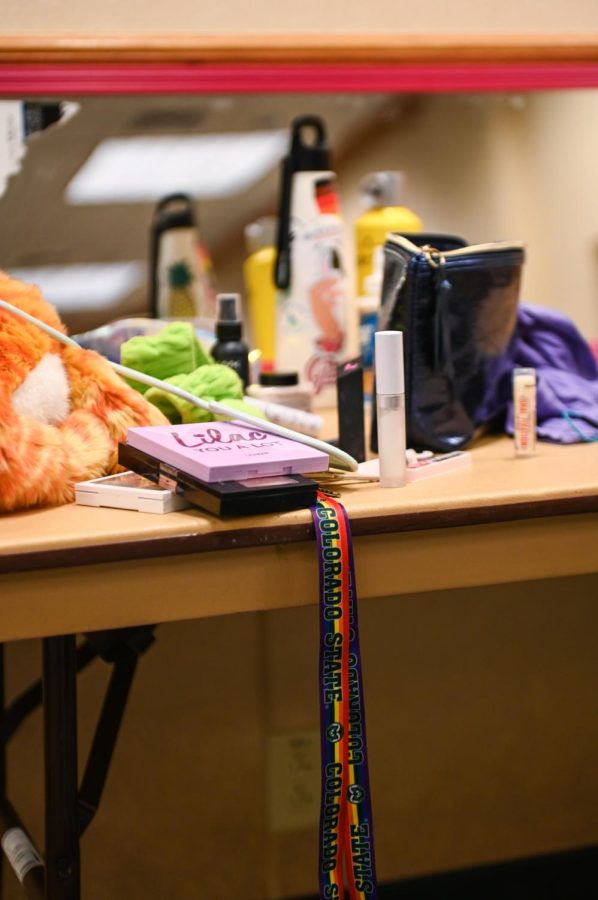 A Colorado State University LGBTQIA+ pride lanyard hangs off of the edge of a drag artist’s makeup station backstage