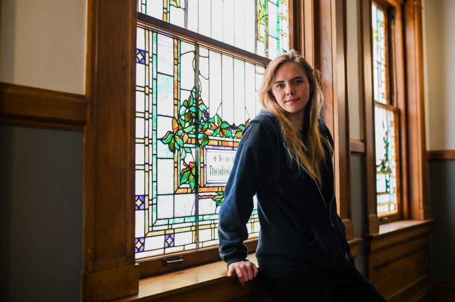 Senior Ren Bergeron stands in front of a stained glass window inside of Guggenheim Hall