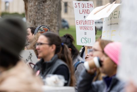 A person in a crowd hold us a sign that says: Stolen Land + Exploited Workers = CSU.