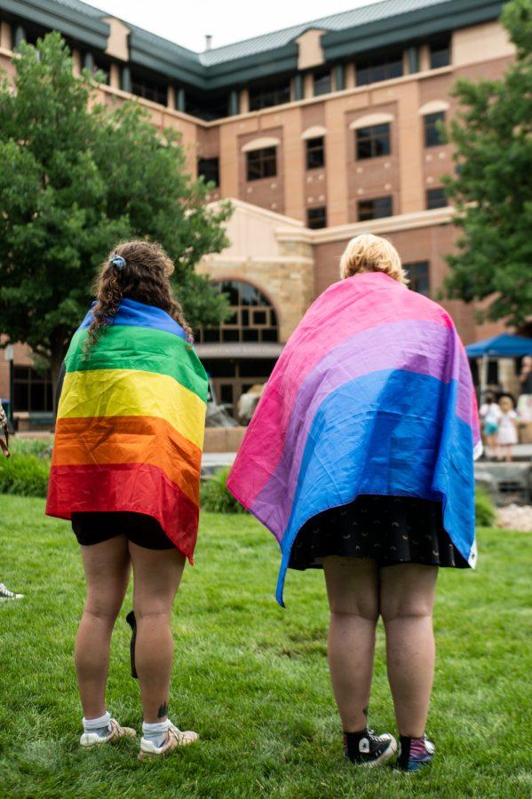 Two festival-goers stand wrapped in Pride flags while they watch performances